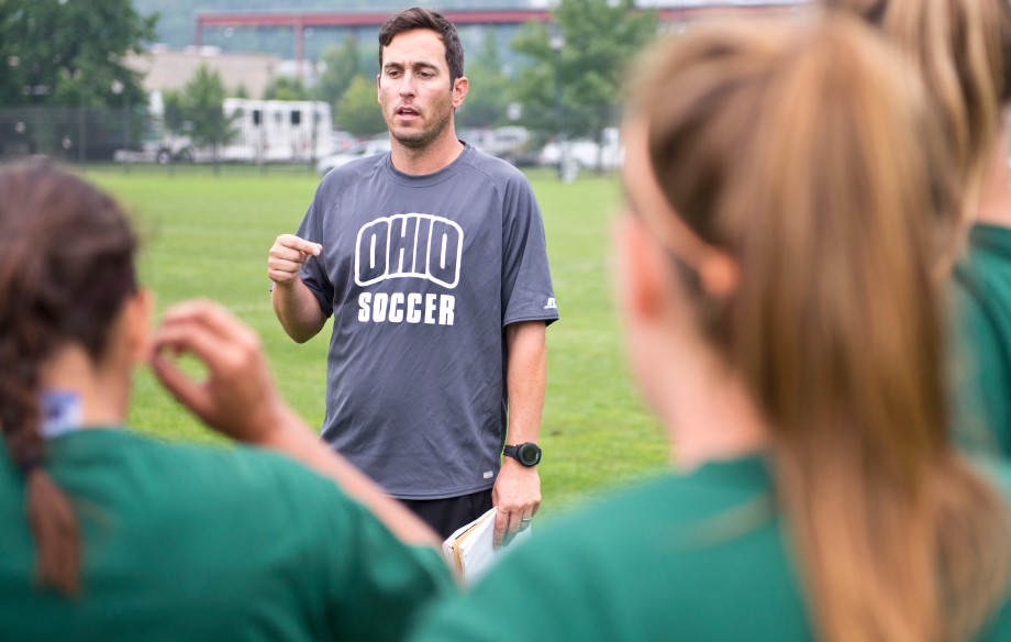 Womens' Soccer head coach Aaron Rodgers talks to players huddled around him Wednesday at practice. (Isaac Hale | Staff Photographer)